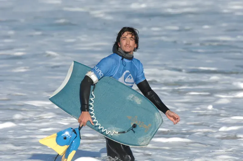Young bodyboarder walking out of the water with board and fins at Capbreton